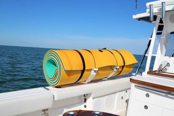 Image of a white FM floating mat storage rack carrying a green and orange floating mat on the side of a boat in the ocean.