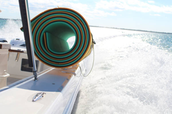 Image of a white FM floating mat storage rack carrying a green and orange floating mat on the side of a boat in the ocean.