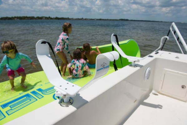 Kids playing on a green and blue floating mat next to a boat that has floating mat storage racks installed on the side.