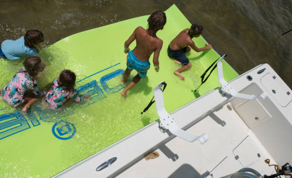 Children playing on a floating mat in the water next to the boat.