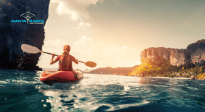 Woman kayaking in the ocean with cliffs and trees on the coastline in the distance.