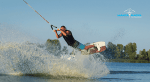 Image of a man wakeboarding on the water with trees behind him on the shore.